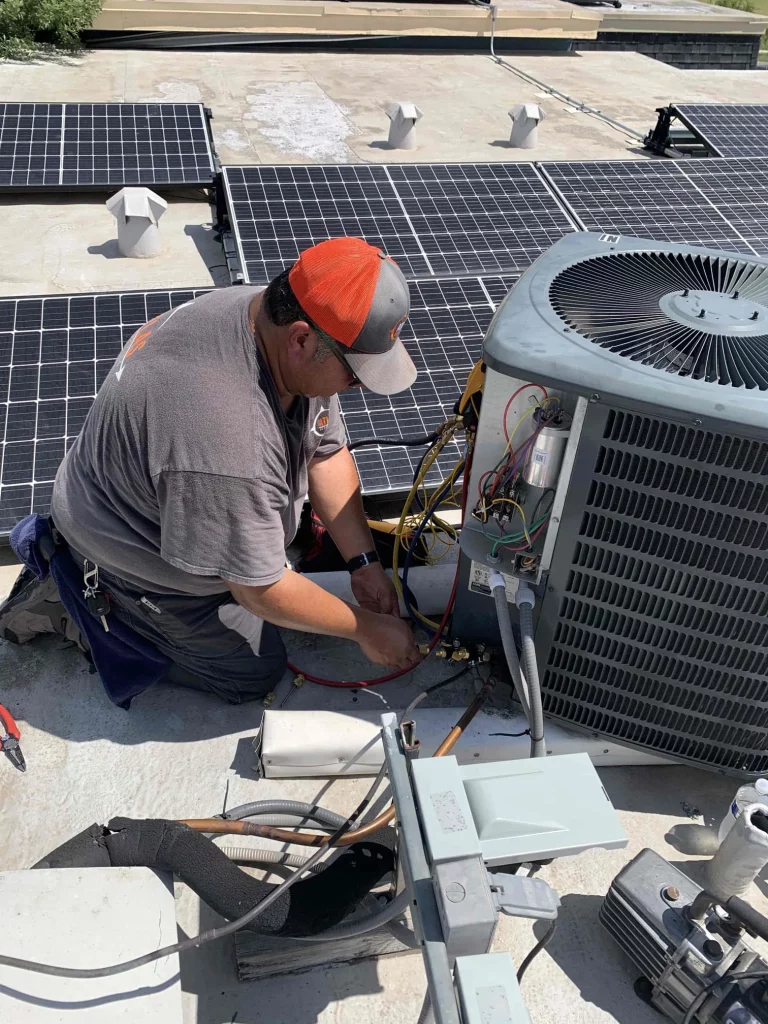 HVAC technician working on air conditioning unit on a commercial rooftop near solar panels.