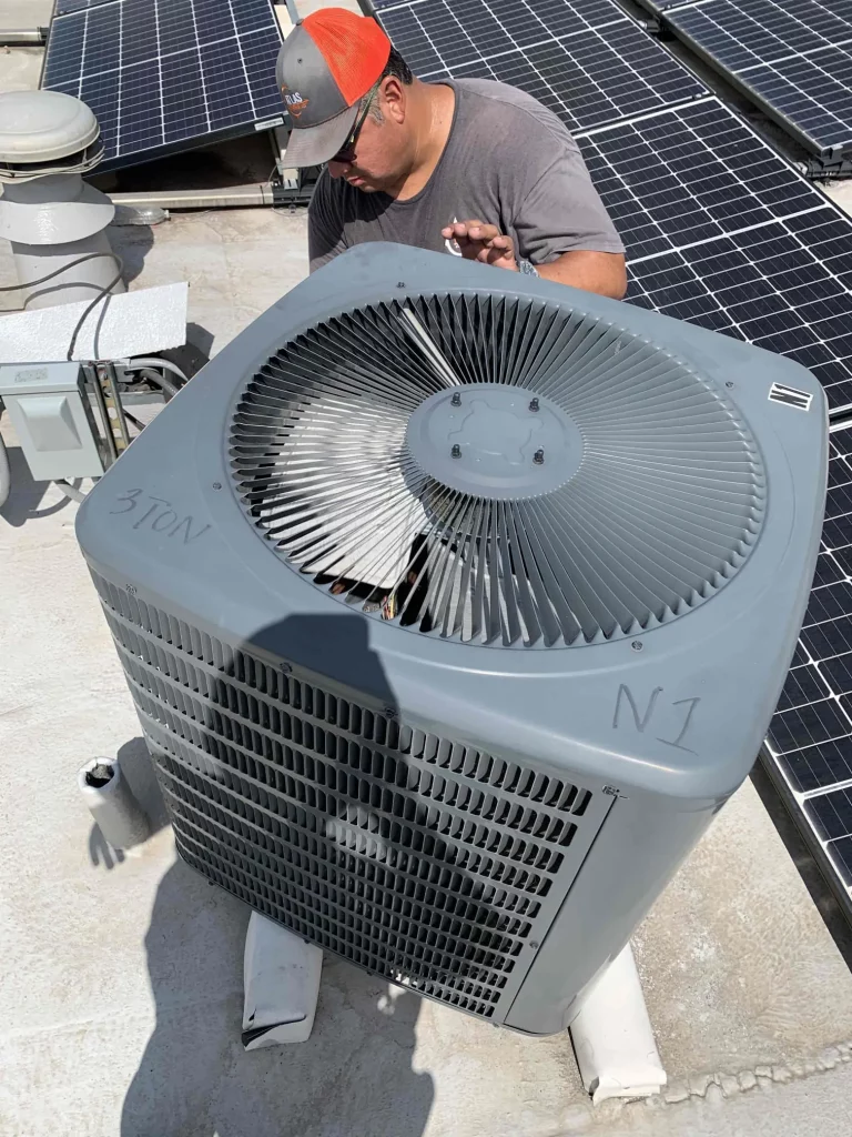 HVAC technician working on AC condenser on a commercial rooftop near solar panels.