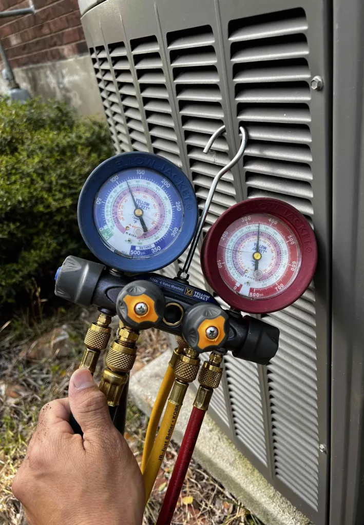 A technician uses manifold gauges, an HVAC diagnostic tool for checking refrigerant pressure, during an AC repair.